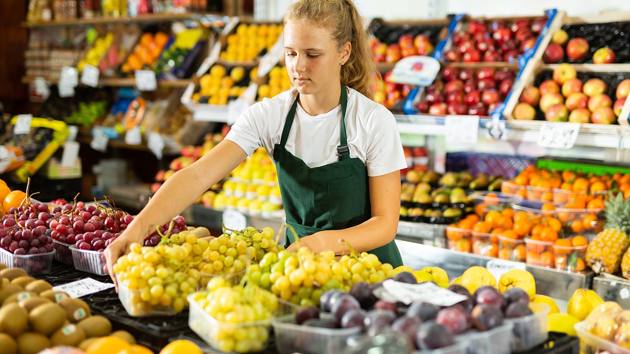 Young salesgirl at her first job, selling green grape and other fruits in vegetable shop