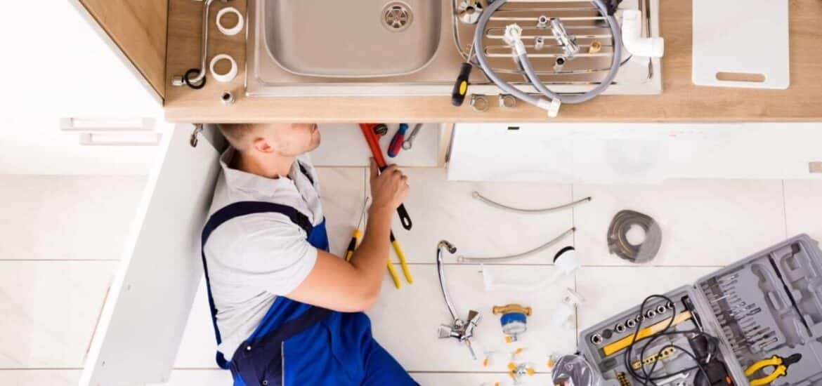 High Angle View Of Male Plumber In Overall Fixing Sink Pipe