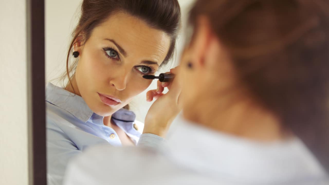 Woman looking in mirror applying mascara