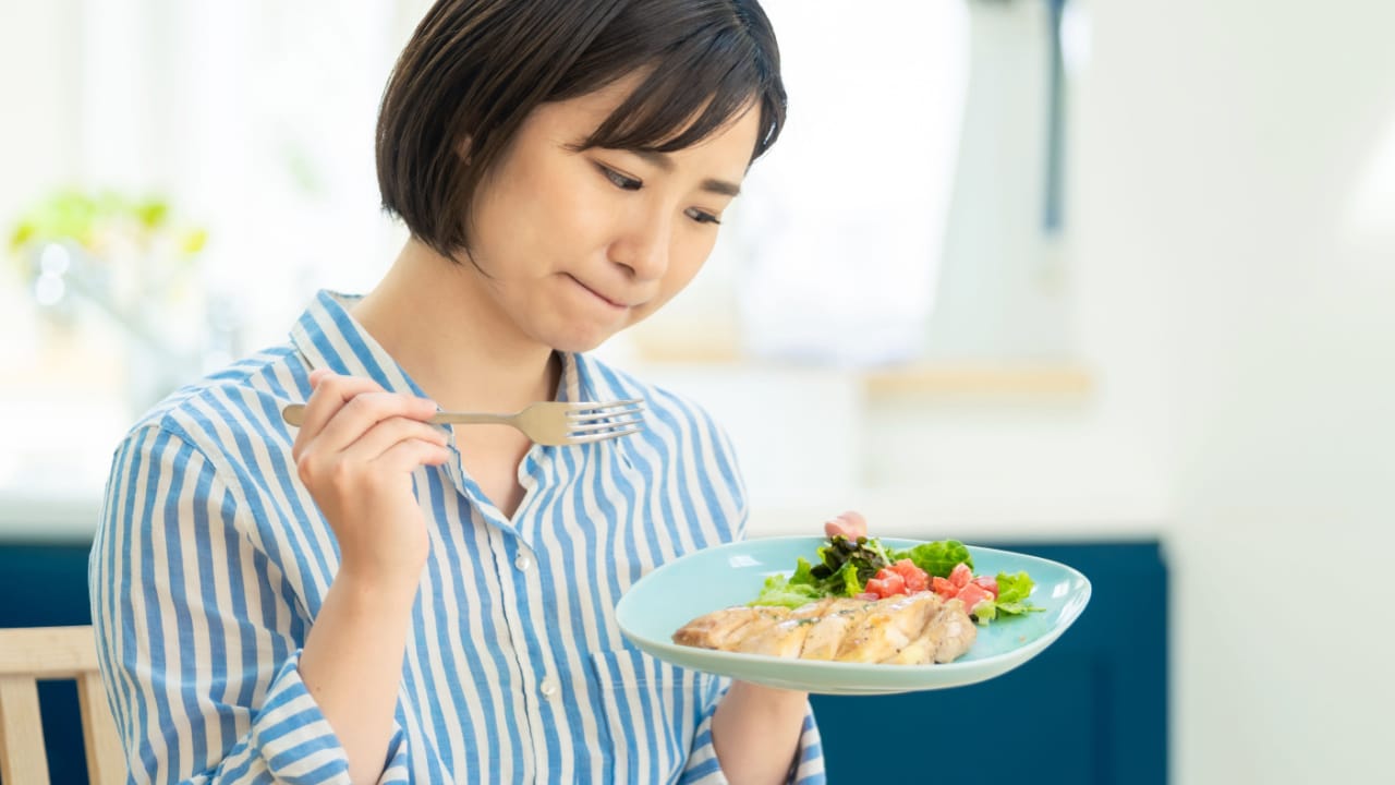 Woman looking unsure at a plate of healthy food.