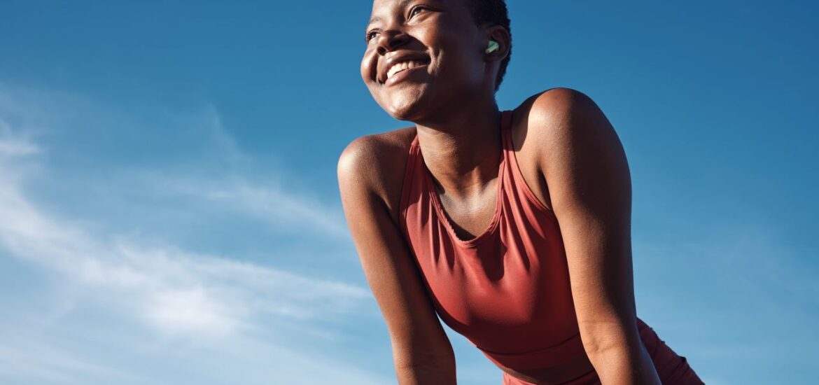 Fitness, black woman and happy athlete smile after running, exercise and marathon training workout. Blue sky, summer sports and run of a African runner breathing with happiness from sport outdoor